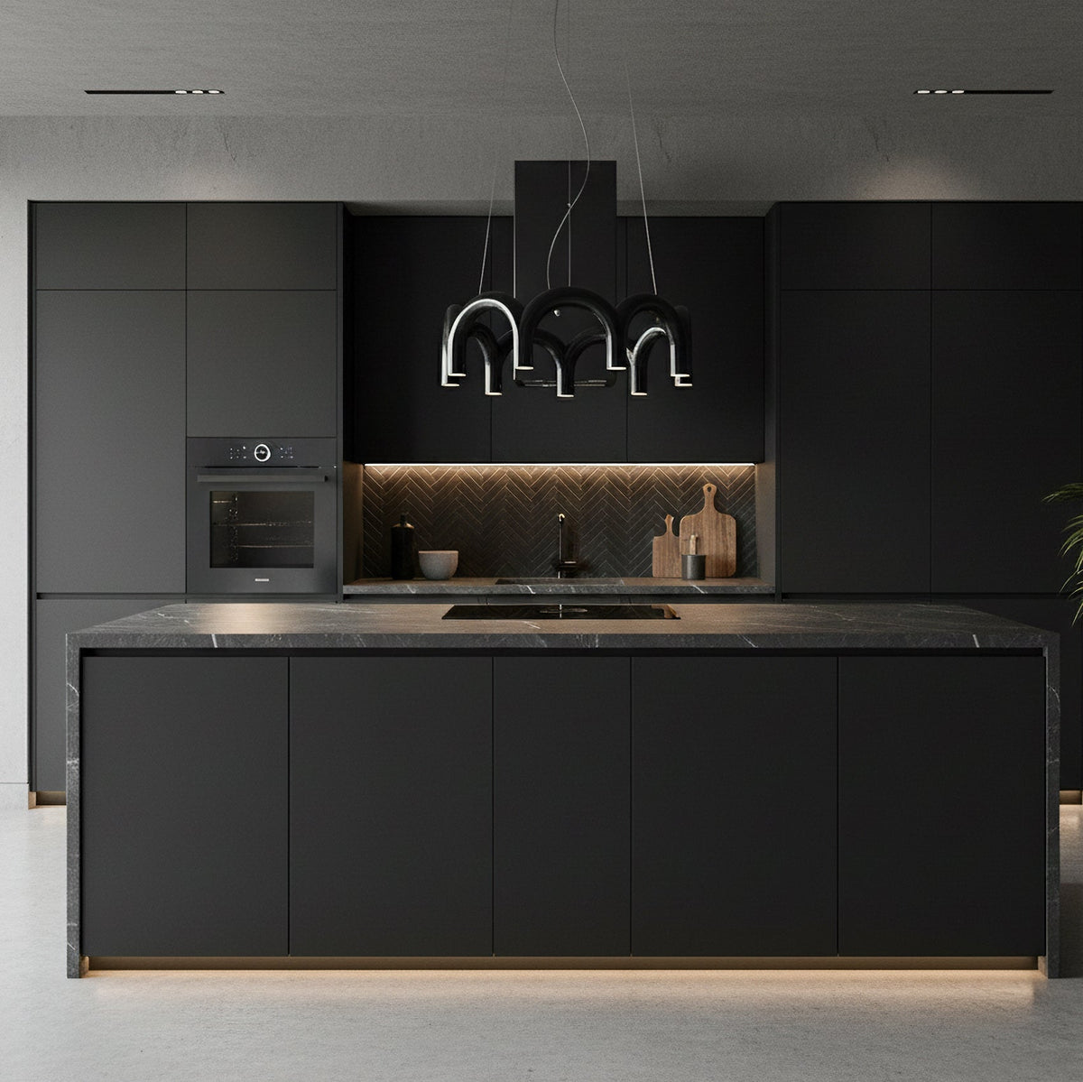 A black Clérachic chandelier with tiered arches above a dark kitchen island, with matching black cabinets behind.