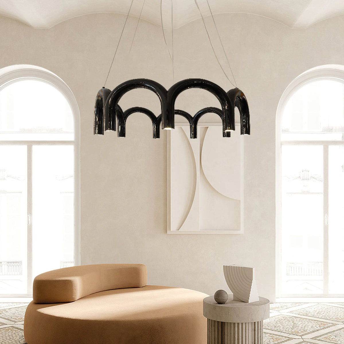 A black tiered-arch Clérachic chandelier in a cream room with arched windows, above a tan curved sofa.