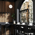 A black arched Clérachic chandelier in a restaurant-style room with timber cladding and a tall arched window.