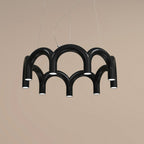 A black tiered-arch Clérachic chandelier on a warm sand-coloured backdrop, with its lights facing down.