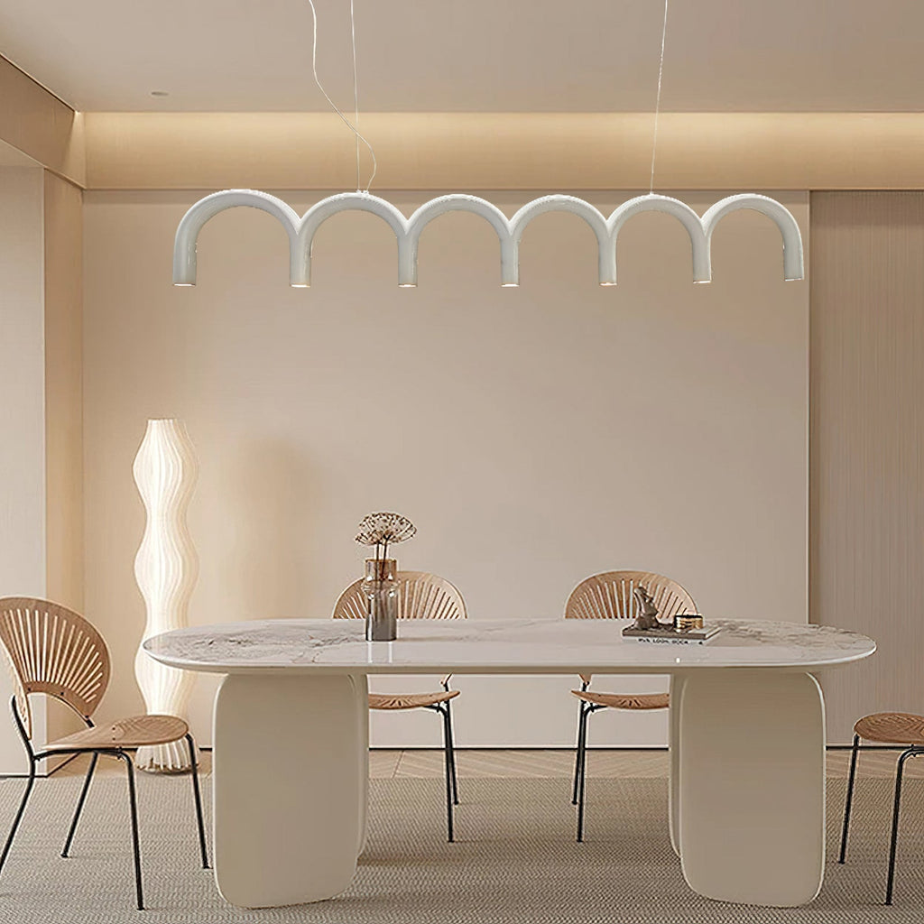 A white arched Clérachic chandelier above a long white dining table with rattan-back chairs and a tall floor lamp.