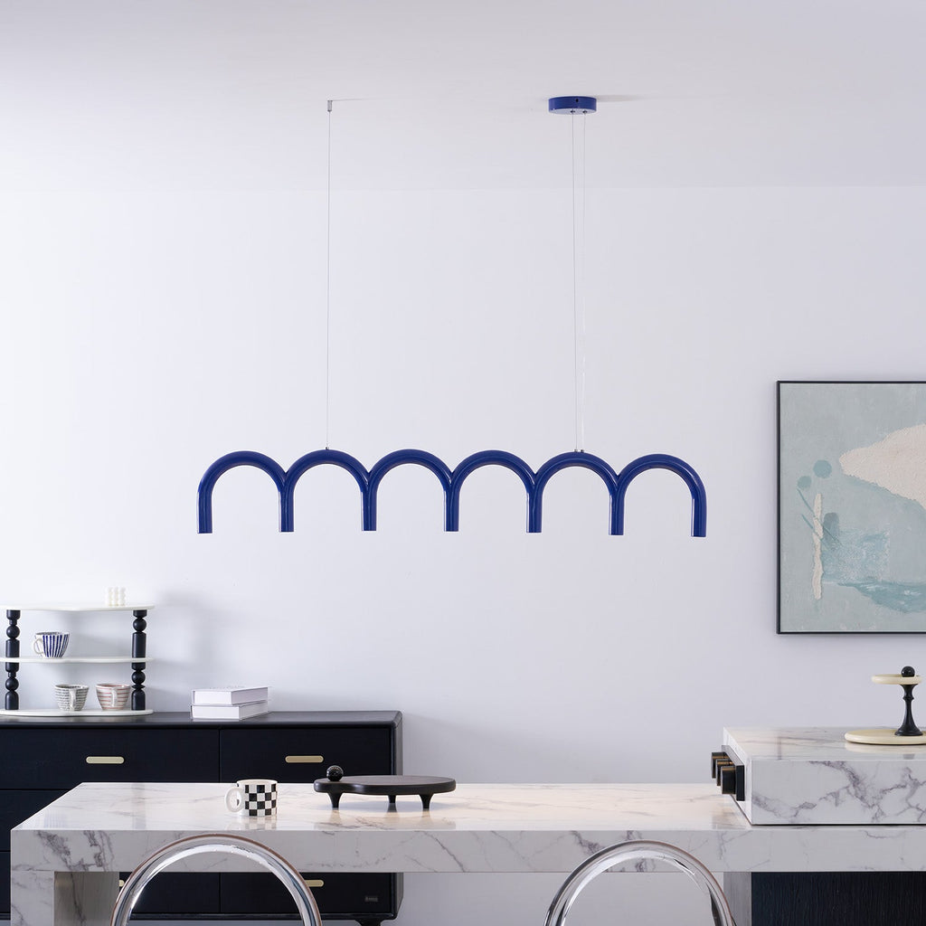 A blue arched Clérachic chandelier above a white marble counter, in front of a white wall and a framed print.
