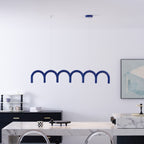 A blue arched Clérachic chandelier above a white marble counter, in front of a white wall and a framed print.
