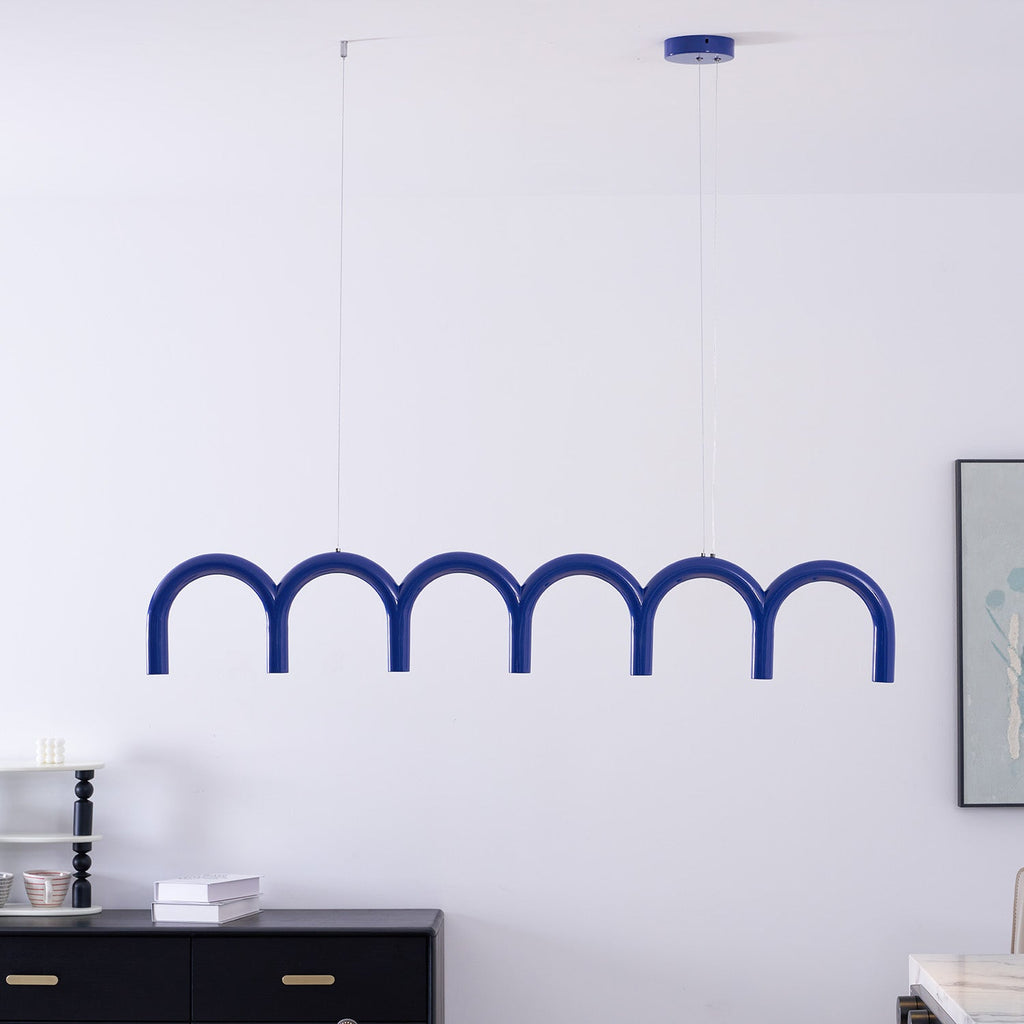 A blue arched Clérachic chandelier hung close to a white wall, with a framed print and a black sideboard behind.