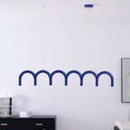 A blue arched Clérachic chandelier hung close to a white wall, with a framed print and a black sideboard behind.