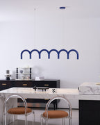 A blue arched Clérachic chandelier above a marble counter with two clear-backed stools with tan seats.