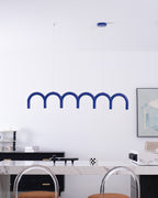 A blue arched Clérachic chandelier seen from a slightly lower angle, with clear-backed stools at the counter below.