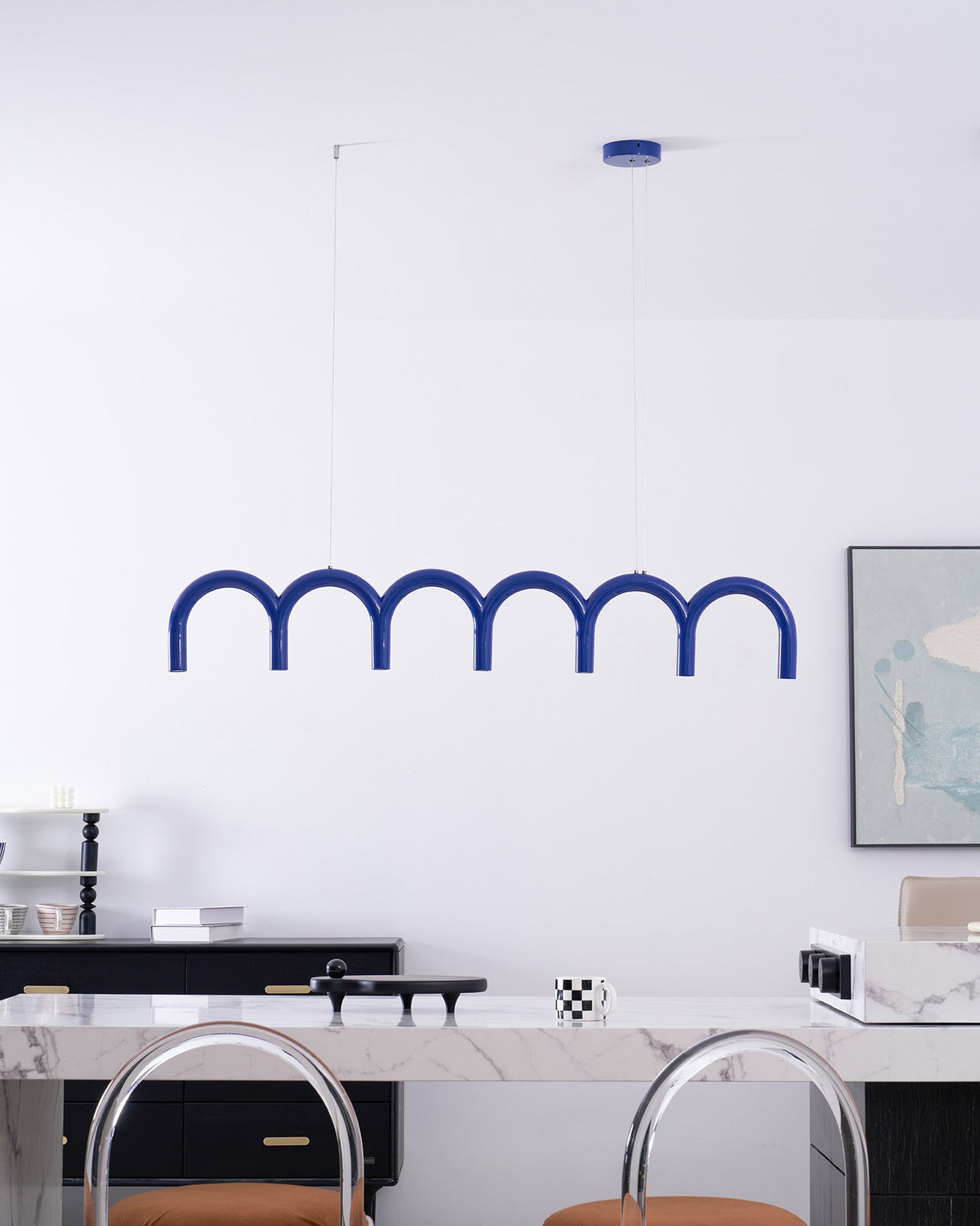 A blue arched Clérachic chandelier seen from a slightly lower angle, with clear-backed stools at the counter below.