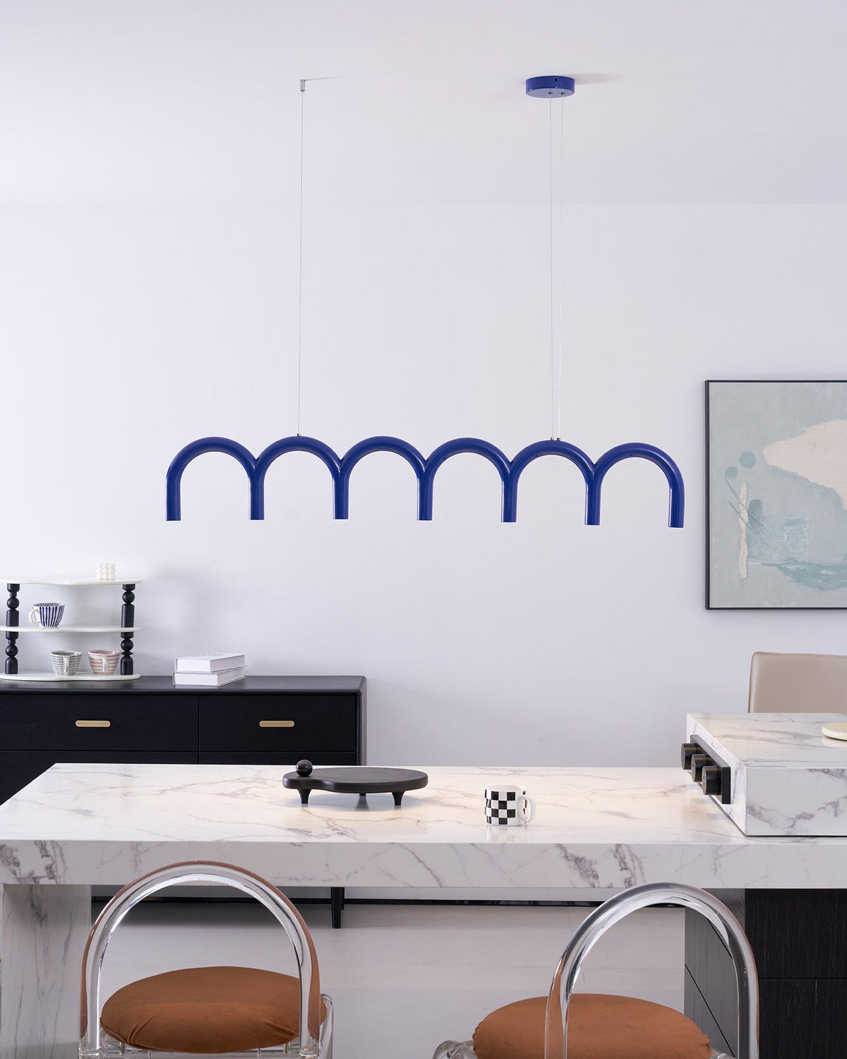 A blue arched Clérachic chandelier above a marble counter and a black sideboard, with a chequered mug on the counter.