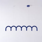 A blue arched Clérachic chandelier with a blue ceiling canopy and two thin cables, against a pale wall.