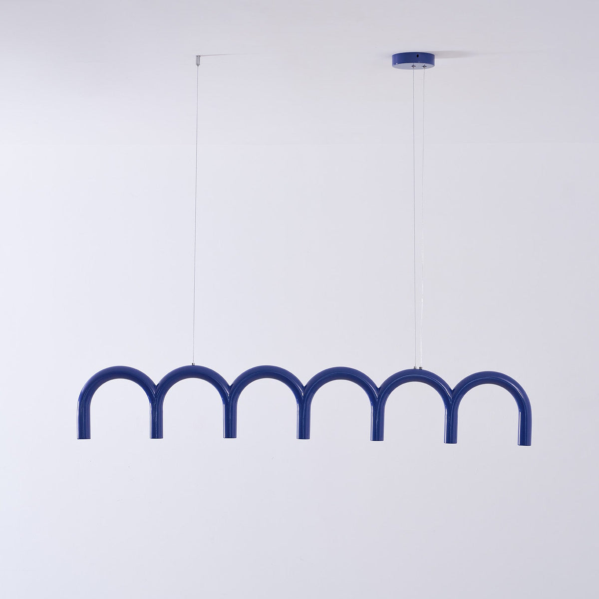 A blue row of arches from this Clérachic chandelier, with a blue canopy and thin cables, against a pale wall.