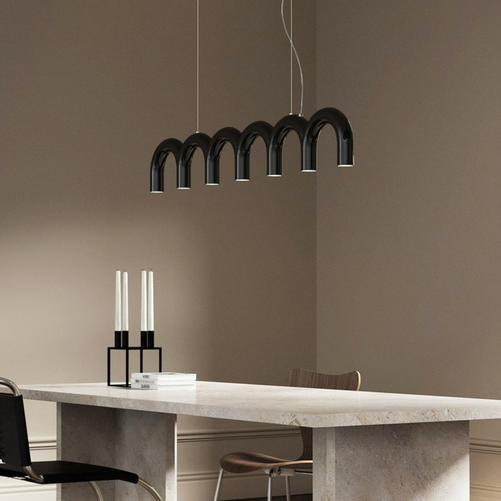 A black arched Clérachic chandelier above a stone dining table, with tall candles and wooden chairs in a taupe room.