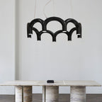 A black tiered-arch Clérachic chandelier above a travertine table, against a pale grey wall.