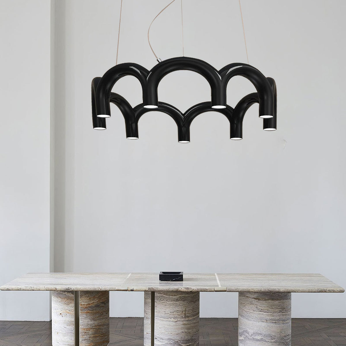 A black tiered-arch Clérachic chandelier above a travertine table, against a pale grey wall.