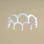 A white tiered-arch Clérachic chandelier hung on three cables, against a warm sand-coloured backdrop.