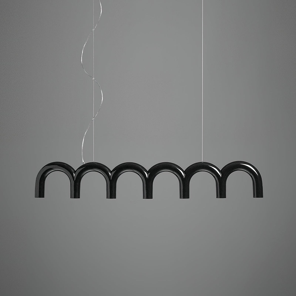 A black row of glossy arches from this Clérachic chandelier, hung on two cables, against a mid-grey backdrop.