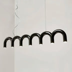 A black arched Clérachic chandelier seen from the side at an angle, with each arch lit and a pale wall behind.