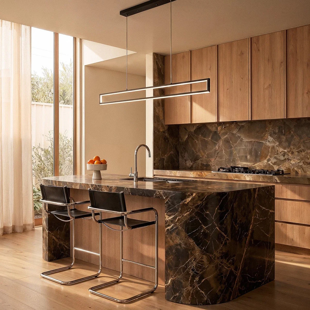 The Clérachic black frame pendant glowing warm white above a marble kitchen island with wood cabinetry.
