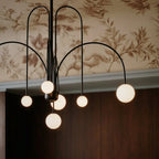 A close view shows the Clérachic chandelier's black looped arms and glowing globes against floral wallpaper.