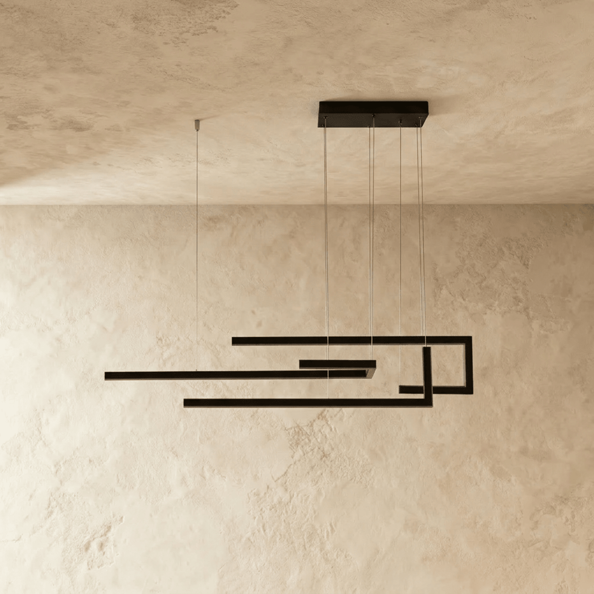 Clérachic's chandelier in black, its angular linear frame glowing softly against a plastered wall.