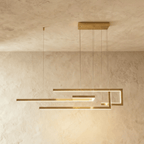 A side view of the Clérachic chandelier in gold, its geometric LED bars glowing warm against a plastered wall.
