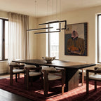 Clérachic's chandelier in black, its geometric bars glowing cool white above a long dining table and rug.