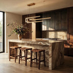 Clérachic's chandelier in gold, its geometric bars glowing warm above a marble kitchen island with stools.