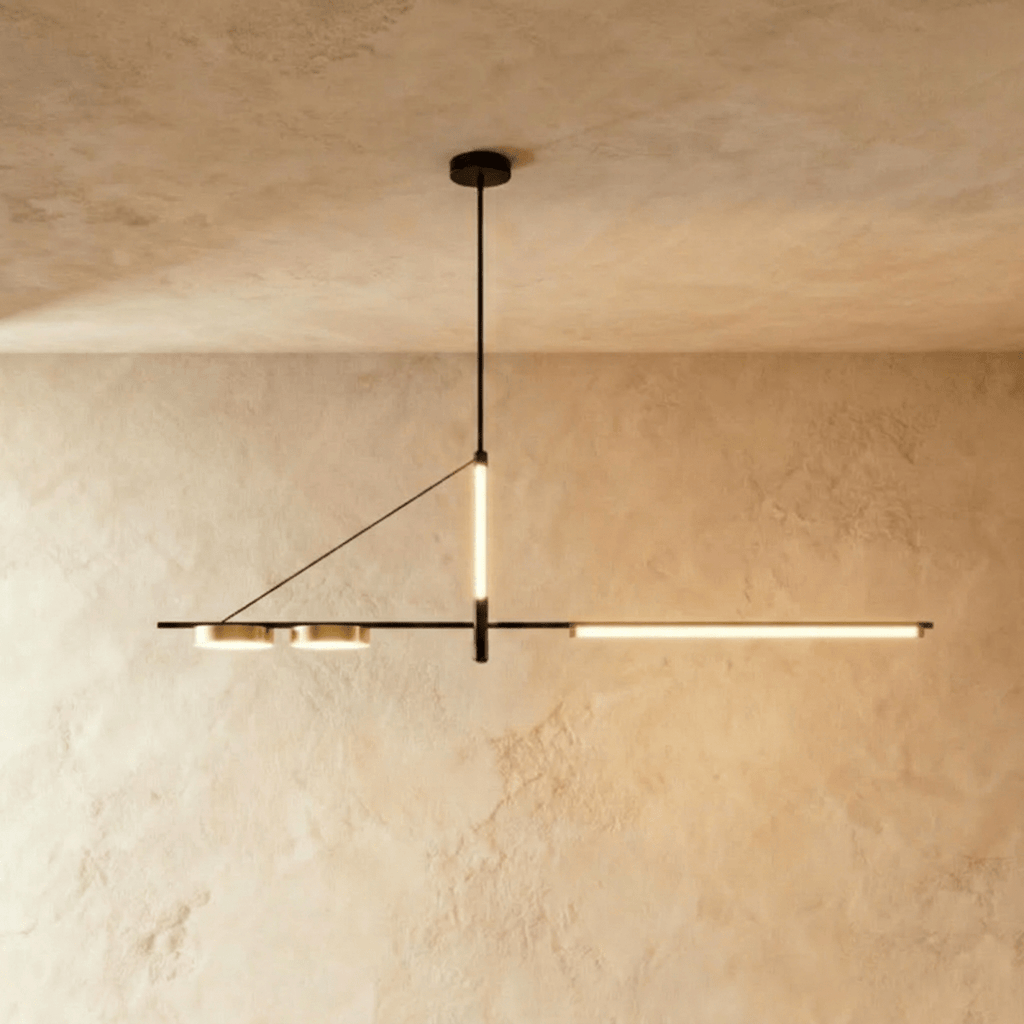 Clérachic slim black linear chandelier on a single rod, with a glowing LED bar and two brass-toned discs, against limewash walls.