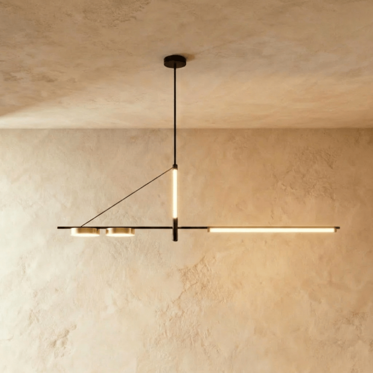 Clérachic slim black linear chandelier on a single rod, with a glowing LED bar and two brass-toned discs, against limewash walls.