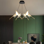 Clérachic bird ring chandelier glowing above a dining table in a room with green panelled walls and a fluted dark wall.