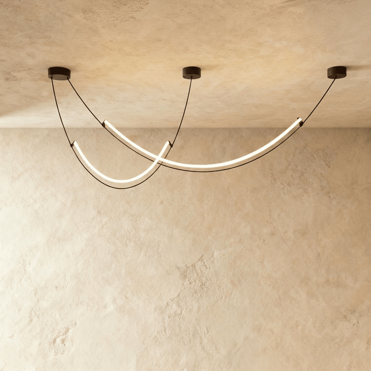 Clérachic chandelier of two slim curved LED arcs hung on black cables from round canopies, lit in a studio against limewash