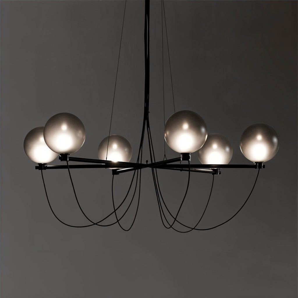 Clérachic chandelier lit against a dark grey backdrop, six frosted smoky globes on black arms with looping cables.