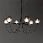 Clérachic chandelier lit against a dark grey backdrop, six frosted smoky globes on black arms with looping cables.