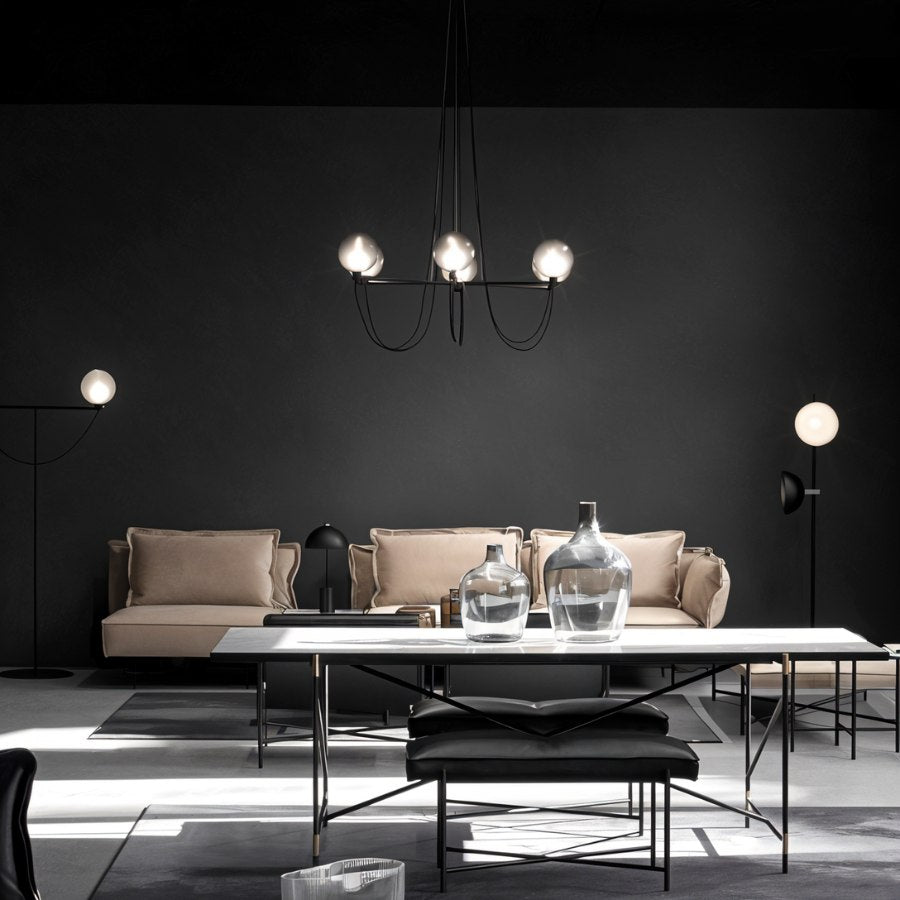 Clérachic six-globe black chandelier above a long dining table in a dark living room with a pale sofa and floor lamps.