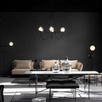 Clérachic six-globe black chandelier above a long dining table in a dark living room with a pale sofa and floor lamps.