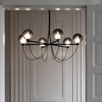 Clérachic lit chandelier with six smoky glass globes framed by a pale panelled doorway, black arms and cables visible.