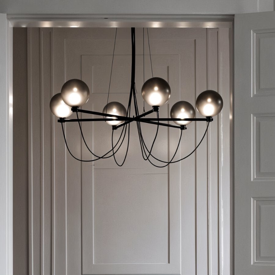 Clérachic lit chandelier with six smoky glass globes framed by a pale panelled doorway, black arms and cables visible.