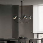 Clérachic black six-globe chandelier hanging low above a dark dining table in a muted grey room beside a bright window.