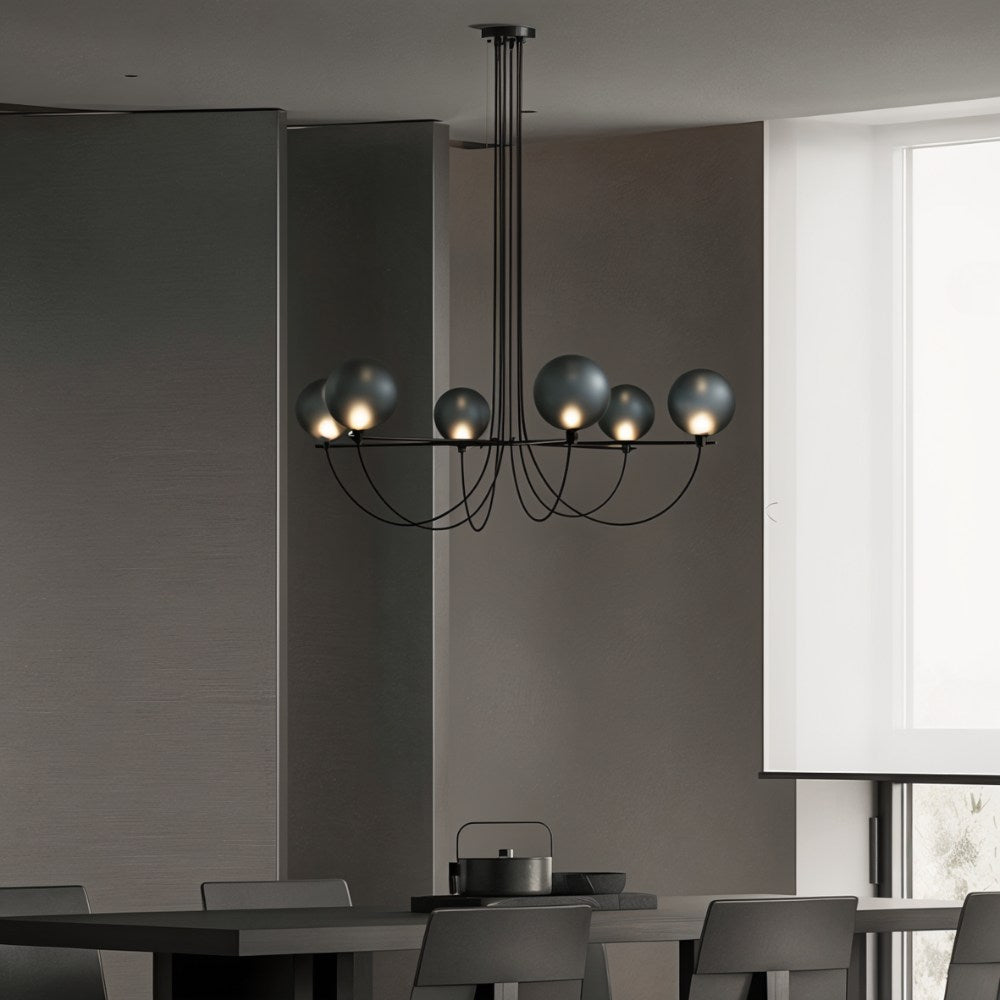 Clérachic black six-globe chandelier hanging low above a dark dining table in a muted grey room beside a bright window.