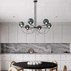 Clérachic six-globe chandelier in blue-grey glass over a round black table in a white kitchen with marble splashback.