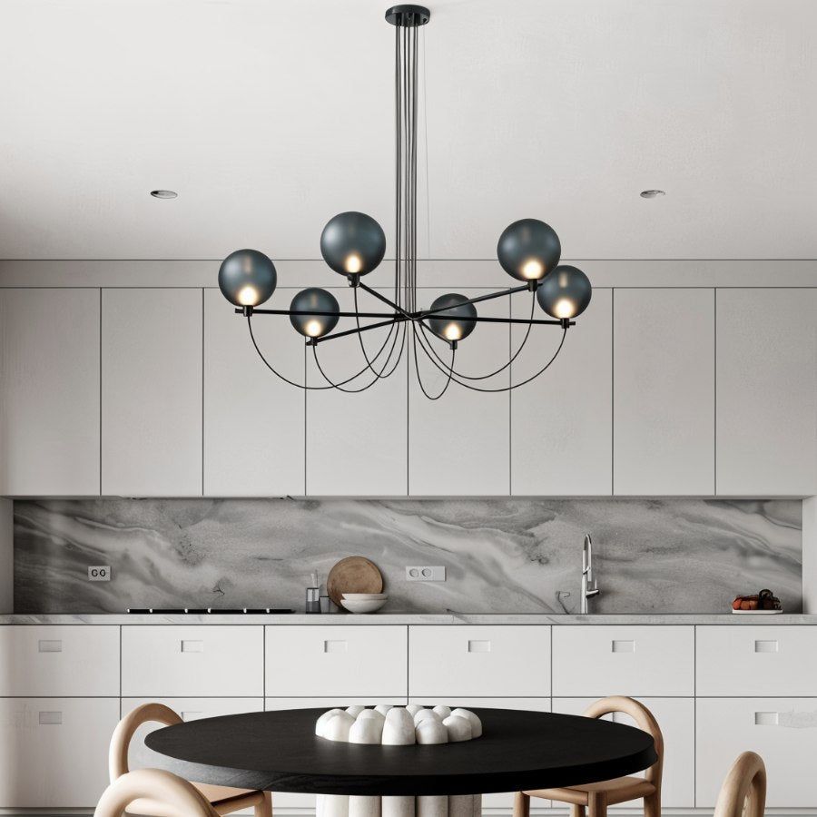 Clérachic six-globe chandelier in blue-grey glass over a round black table in a white kitchen with marble splashback.