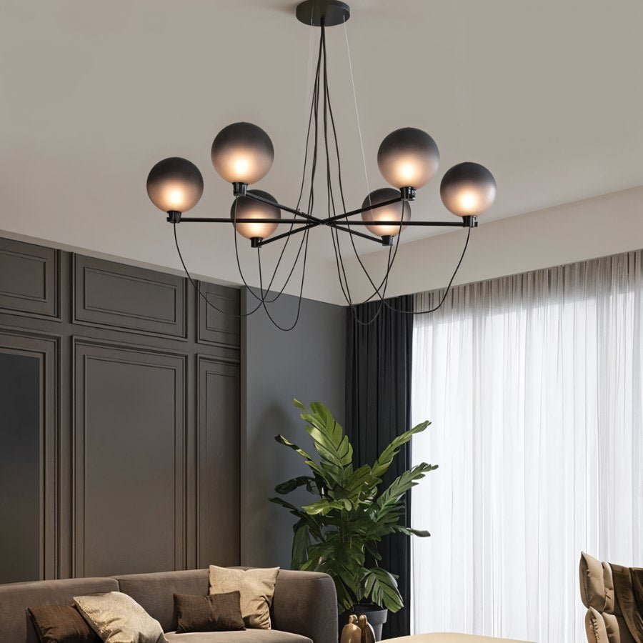 Clérachic chandelier with graduated smoky glass globes glowing in a living room with panelled grey walls and sheer curtains.