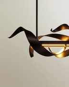 Clérachic close view of a black steel ribbon curling around a warm LED bar, the inner face showing a gold tone.