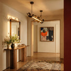 Clérachic black ribbon chandelier lit warm above a hallway with a walnut console, mirror, framed painting and patterned rug.