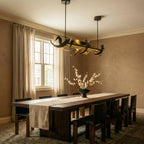 Clérachic black ribbon chandelier on two rods above a long walnut dining table with linen runner and white blossom in a bowl.
