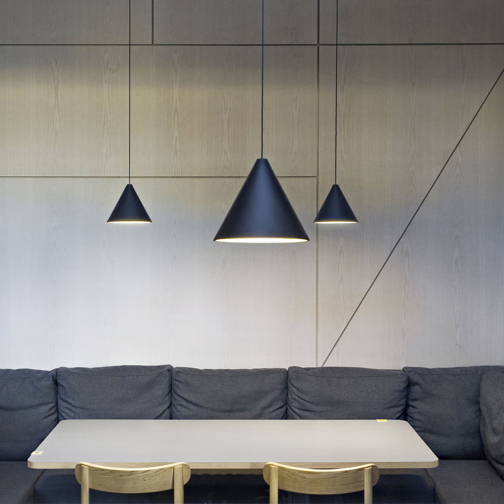 Three Clérachic black cone pendants at different heights over a pale table and a grey banquette, against a wood-panelled wall.