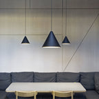Three Clérachic black cone pendants at different heights over a pale table and a grey banquette, against a wood-panelled wall.