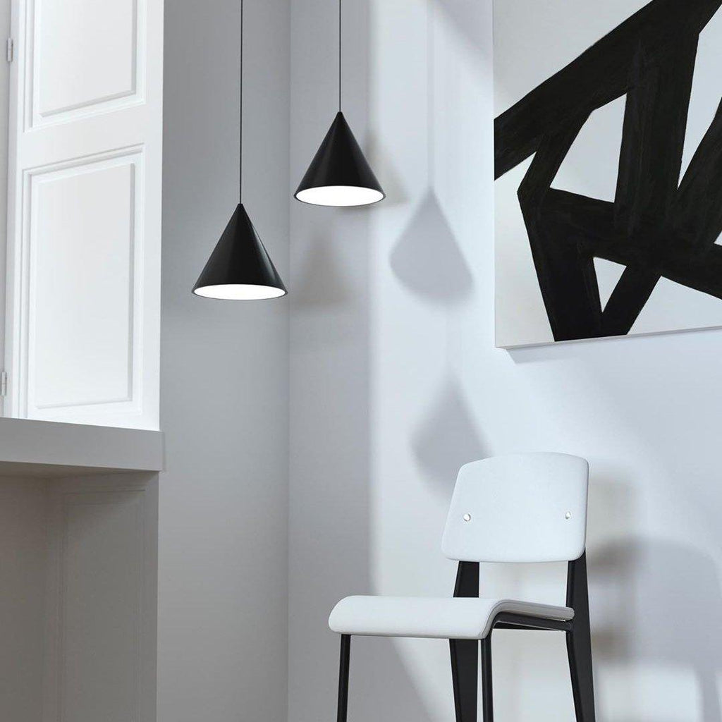 Two black cone pendants from Clérachic hang beside a tall white wall with a bold black-and-white painting and a white chair.