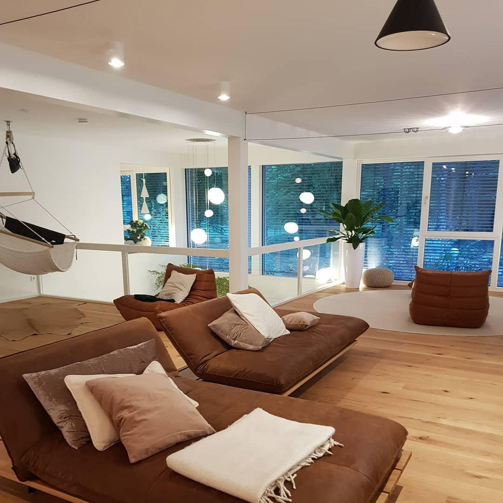 A black cone from Clérachic hangs at the top of a loft living room with brown sofas, oak floors and glass sphere lights beyond.