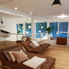 A black cone from Clérachic hangs at the top of a loft living room with brown sofas, oak floors and glass sphere lights beyond.